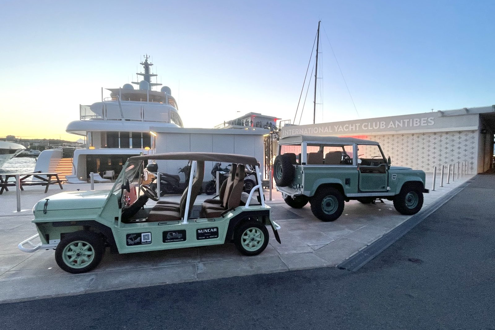 Moke électrique verte et Land Rover Defender vert SUNCAR au coucher de soleil à l'International Yacht Club d'Antibes