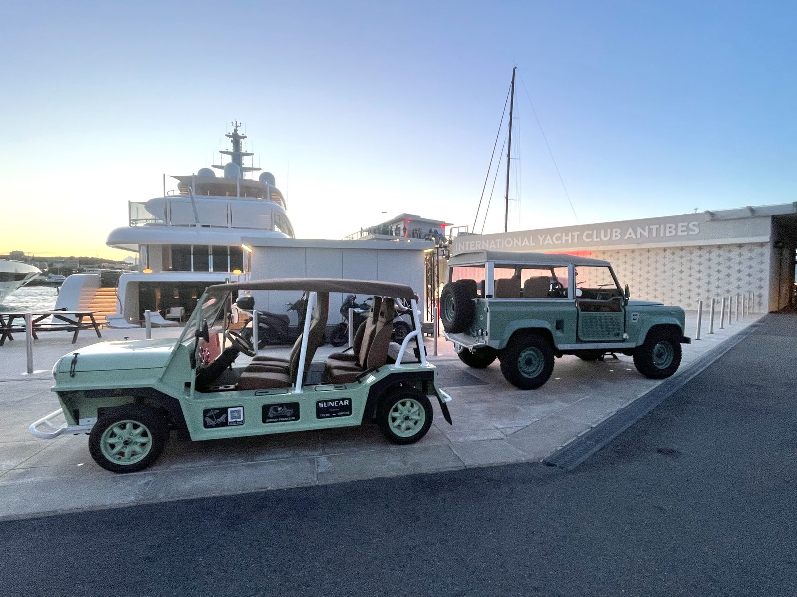 Moke électrique verte et Land Rover Defender vert SUNCAR au coucher de soleil à l'International Yacht Club d'Antibes