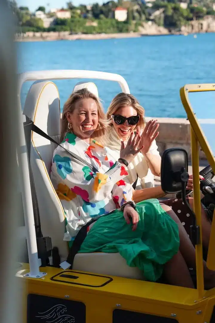 Deux amies rient à bord d'une Moke électrique jaune au bord de la mer