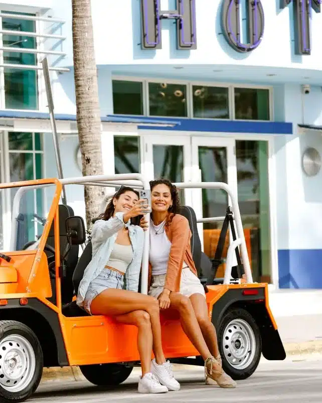 Deux amies prennent un selfie devant une Moke électrique orange