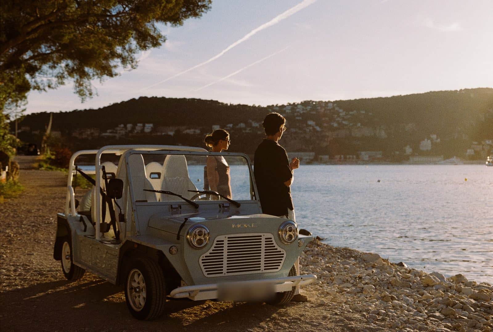 Moke électrique à ciel ouvert en bord de mer à l'heure dorée, un couple à côté